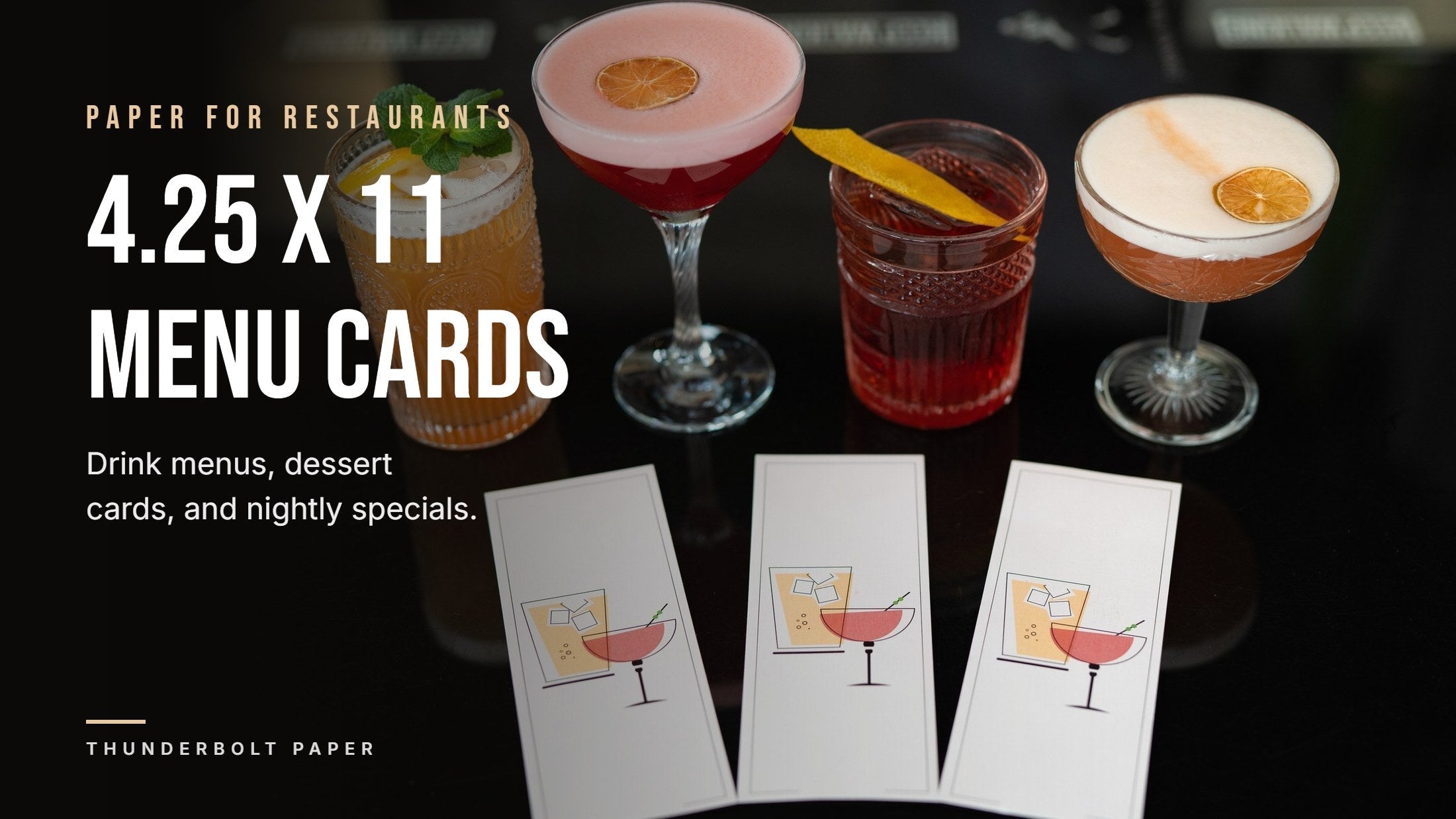 Three printed 4.25 x 11 cocktail menu cards on a dark bar below four cocktails